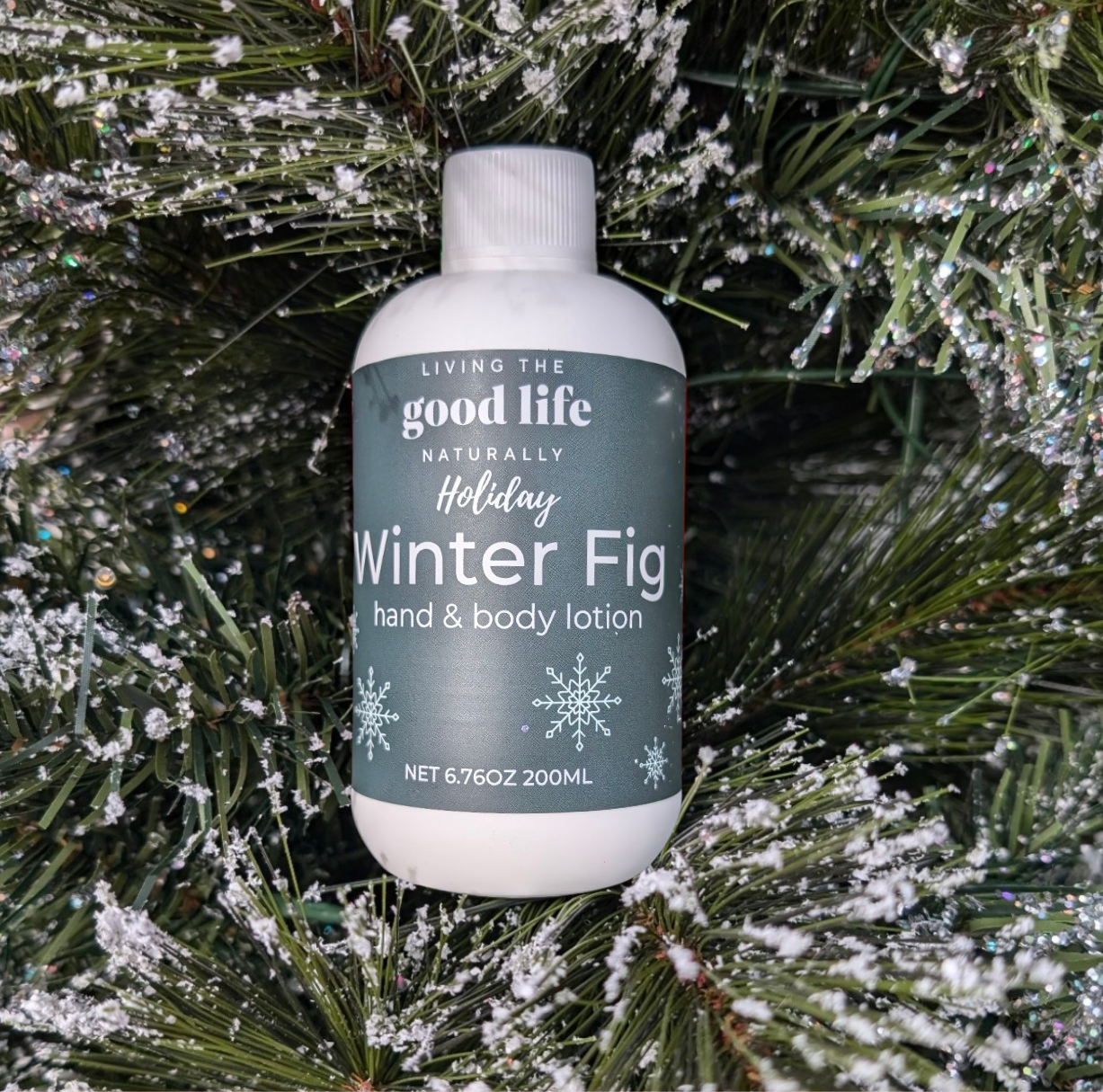 Snowy Christmas limbs with a handmade bottle of Winter Fig Lotion with a green label